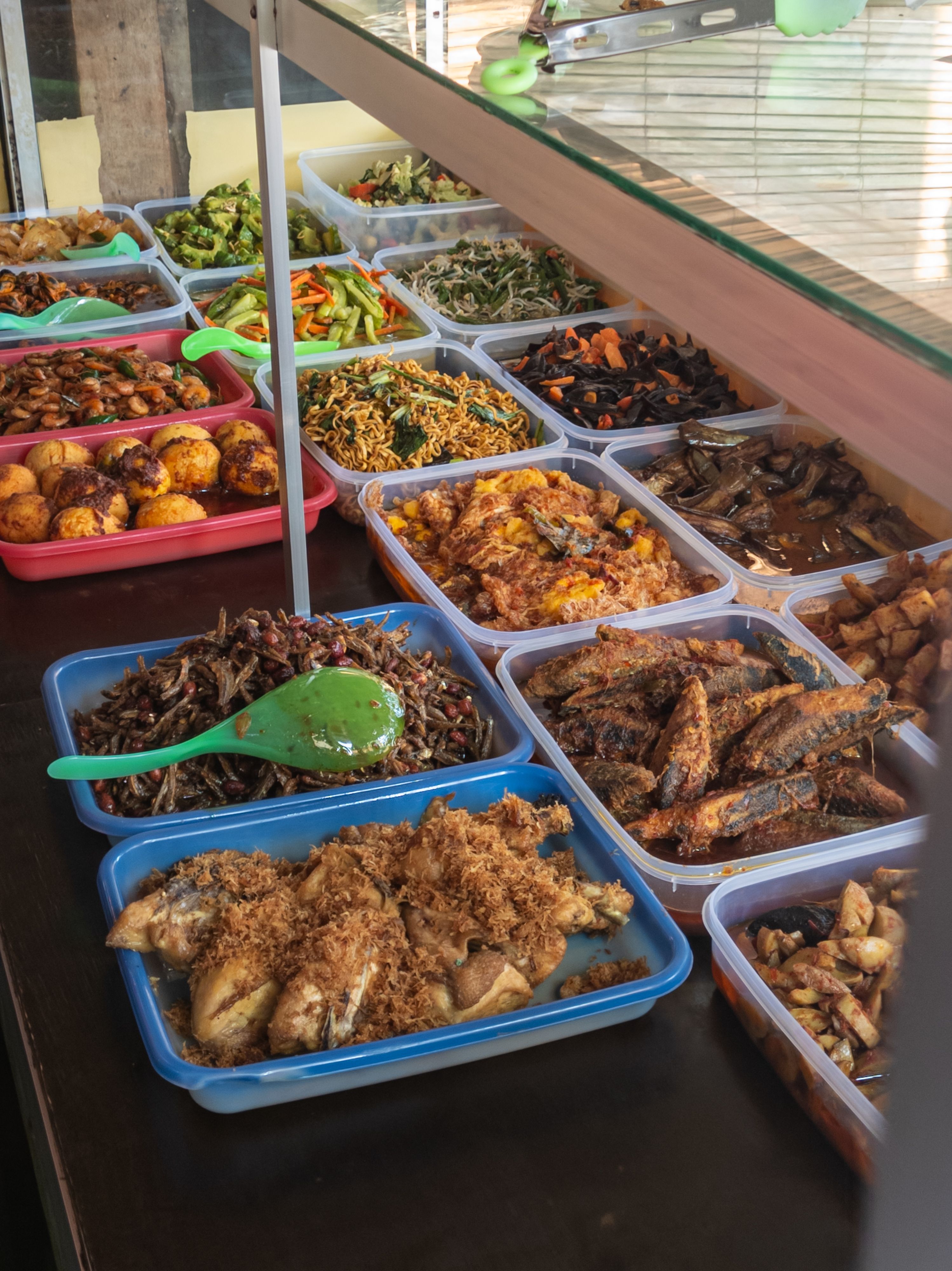 A colourful spread of traditional Balinese warung dishes displayed behind a glass counter